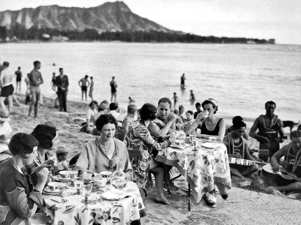 People enjoying their lunch served at tables on the beach in front of the Royal Hawaiian Hotel on Waikiki Beach, Honolulu, Hawaii, circa 1936.