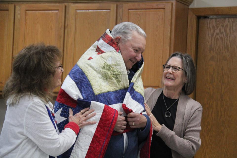 Members of the Perry Piecemakers help wrap David Oliveira in a Quilt of Valor during a presentation on on Friday, Nov. 10, 2023, at the Perry Elks Lodge.