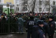 Interior Ministry members stand guard as bystanders and relatives of students gather behind a fence near a high school, where a student shot a teacher and a police officer dead and held more than 20 other students hostage, on the outskirts of Moscow, February 3, 2014. The student was disarmed and detained, police said, just days before Russia hosts the Winter Olympics. (REUTERS/Maxim Shemetov)