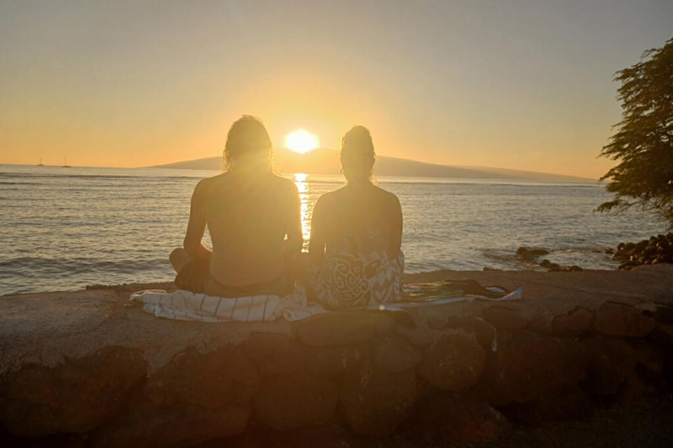 In this January 2023 photo provided by Sherrie Esquivel, right, she sits with her father, Thomas Leonard, on the seawall in Lahaina, Hawaii, watching the sunset. Esquivel, of Dunn, N.C., spent frantic days trying to find her father after fires devastated Lahaina this week. Neighbors told her early Friday, Aug. 11, 2023, he was safe, and she only found out ordeals of how he survived by reading an Associated Press article. (Courtesy of Sherrie Esquivel via AP)