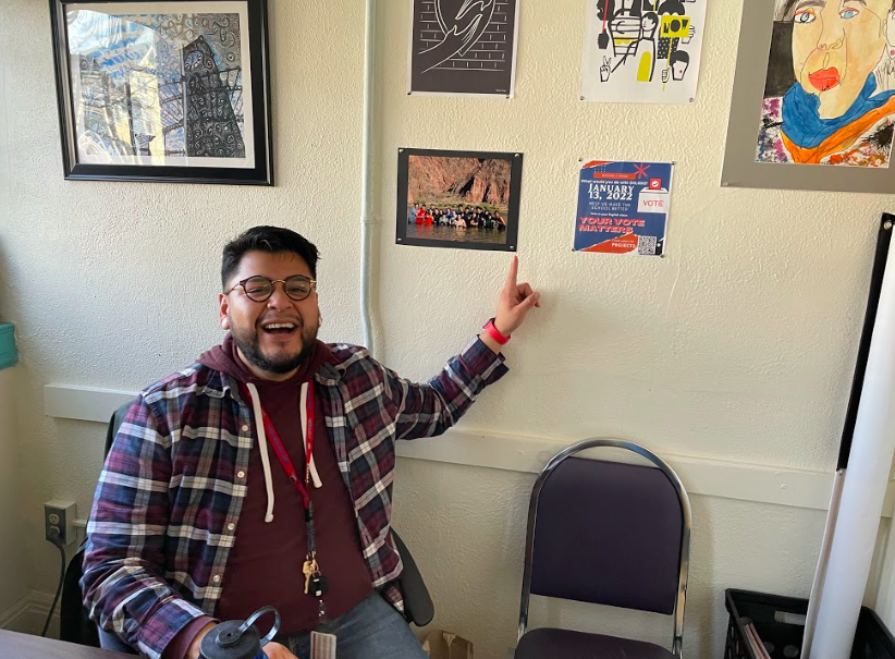 Teacher Emmanuel Ramos in his office where a poster encouraging students to vote on a class winning project hangs on the wall. (Asher Lehrer-Small)
