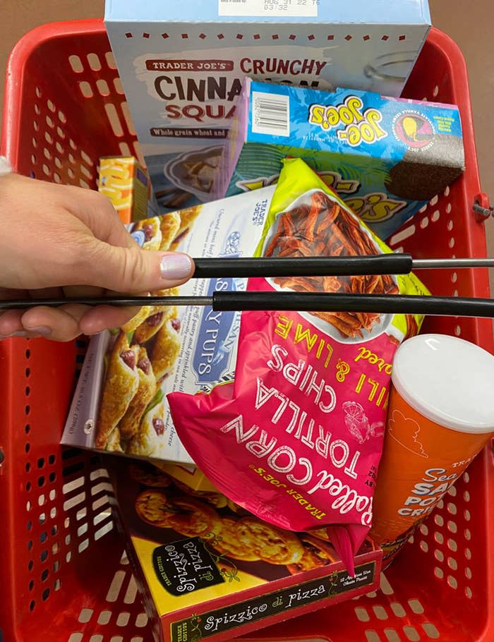 A hand holding a grocery cart full of food.