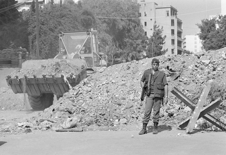 FILE - While a French trooper stands guard, an earth mover constructs a block of a street to beef up security near French paratroop command two days after it was attacked by a terrorist bomb, in Beirut, Tuesday, Oct. 25, 1983. Judicial authorities in France have sent a judicial request to Lebanon's prosecution, Wednesday, March 8, 2023, asking them to detain two people suspected in being involved in a 1983 bombing in Beirut that killed dozens of French troops, judicial officials said Wednesday. (AP Photo/Azakir, File)