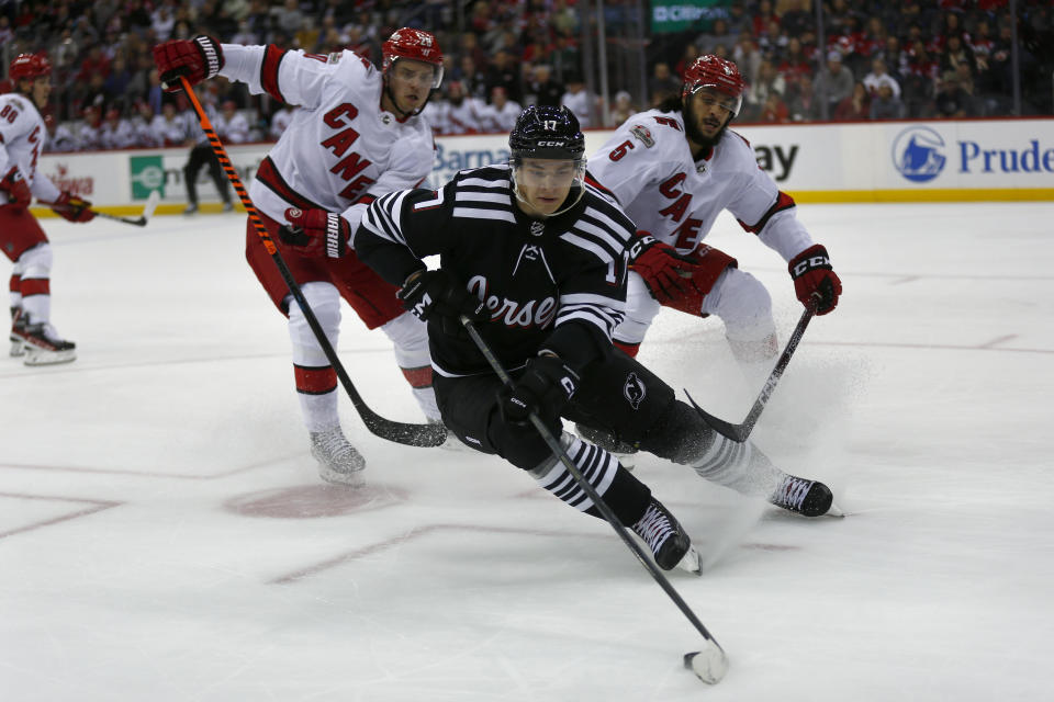 New Jersey Devils center Yegor Sharangovich skates away from Carolina Hurricanes center Sebastian Aho, left, and defenseman Jalen Chatfield during the first period of an NHL hockey game, Sunday, Jan. 1, 2023, in Newark, N.J. (AP Photo/John Munson)