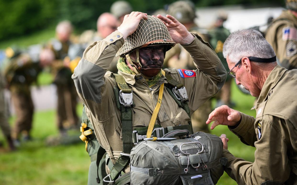 Parachutists wearing replica WWII-era paratrooper attire check their equipment prior to their jump from a Lockheed C-130 Hercules aircraft