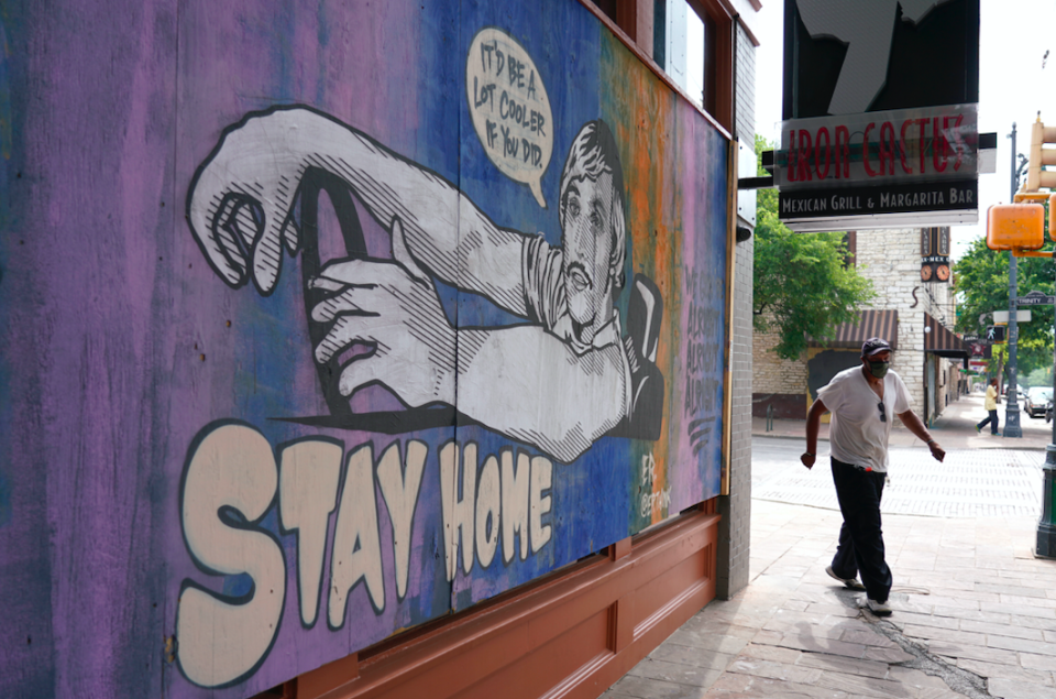 A man walks past a mural painted over wood used to board up a closed business on Sixth Street in Austin, Texas. (PA)