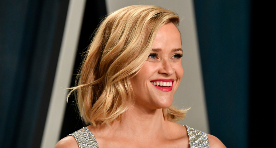 Reese Witherspoon smiling on red carpet with red lipstick and silver dress straps