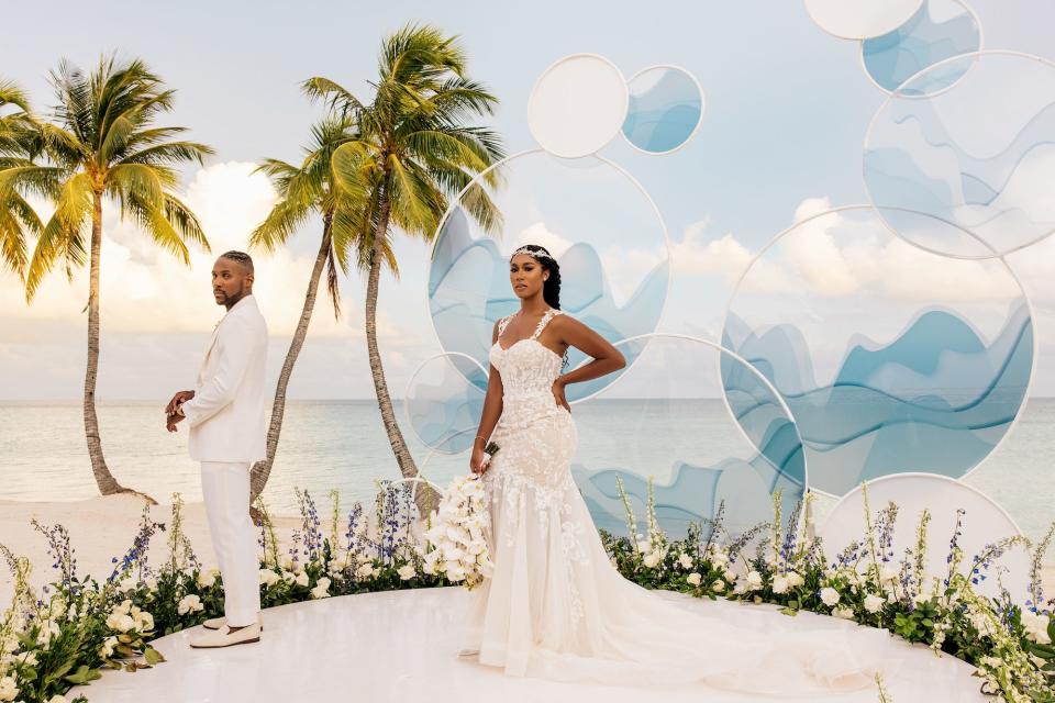 A bride and groom pose in front of a dramatic backdrop.