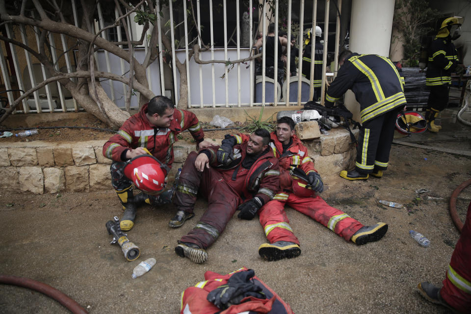 Lebanese firemen rest outside a building that was burned in a wildfire overnight, in the town of Damour, just over 15km (9 miles) south of Beirut, Lebanon, Tuesday, Oct. 15, 2019. Strong fires spread in different parts of Lebanon forcing some residents to flee their homes in the middle of the night as the flames reached residential areas in villages south of Beirut. (AP Photo/Hassan Ammar)