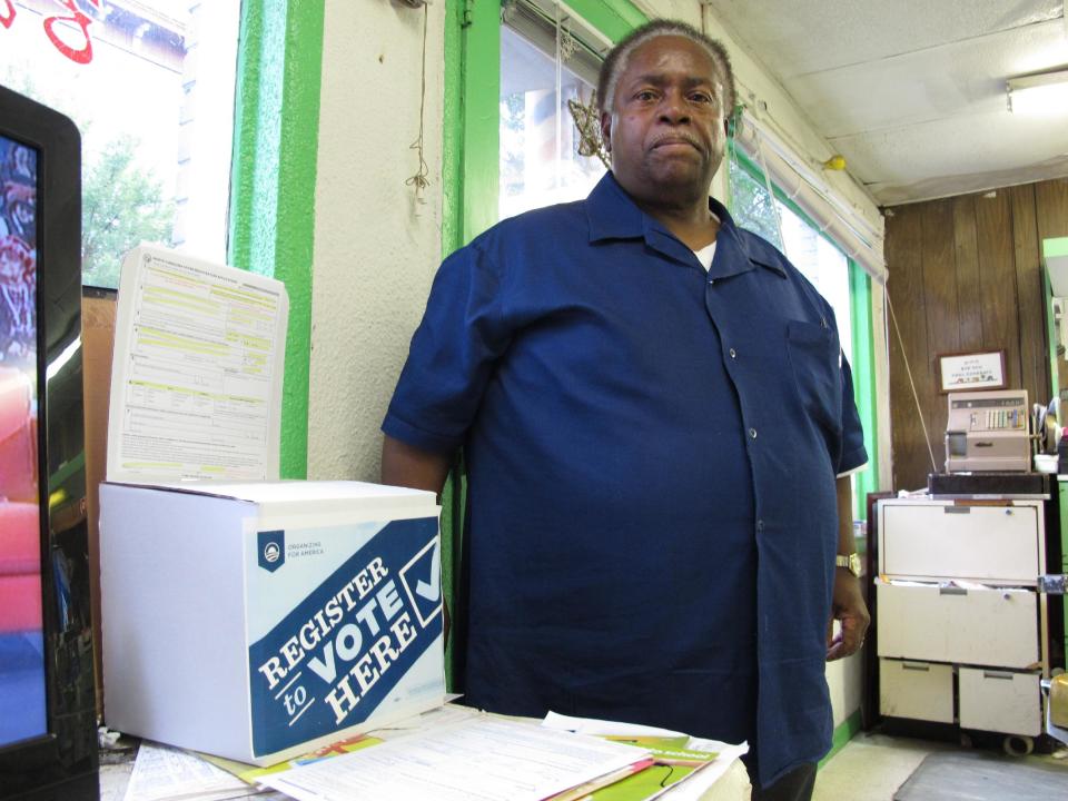 In this Wednesday, Aug. 22, 2012 photo, barber Carlton Nicholson stands beside a voter registration box in his downtown Raleigh, N.C. shop. President Barack Obama's campaign placed hundreds of these boxes in black-owned businesses in hopes of repeating his historic win in this conservative swing state. Nicholson voted for Obama in 2008 and plans to do so again, but he says it's going to take more than a few hundred boxes to keep North Carolina from crossing back over into the red column. (AP Photo/Allen Breed)