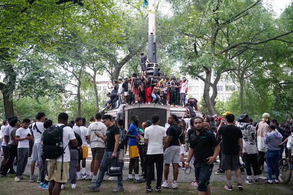 People climb a sculpture, Friday, Aug. 4, 2023, in New York's Union Square. Police in New York City struggled to control a crowd a crowd of thousands of people who gathered in Manhattan's Union Square for an Internet personality's videogame console giveaway that got out of hand.