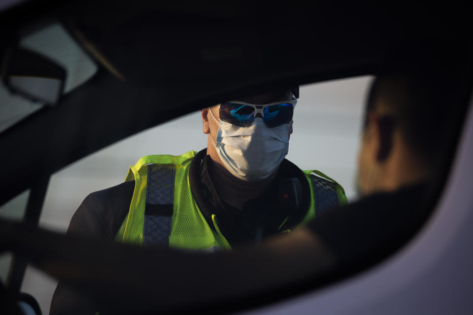 An Israeli police officer wears a face mask amid concerns over the country's coronavirus outbreak as he checks the documents of a driver at a checkpoint on a freeway near Hadera, Israel, Tuesday, April 28, 2020. Israel's government announced a complete lockdown over the upcoming Israel's 72nd Independence Day to control the country's coronavirus outbreak. (AP Photo/Ariel Schalit)
