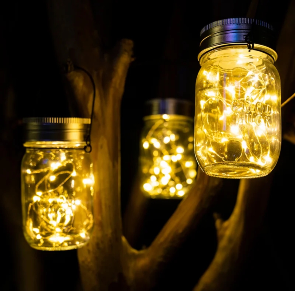 Three mason jar lanterns with lights inside hanging from a small garden tree