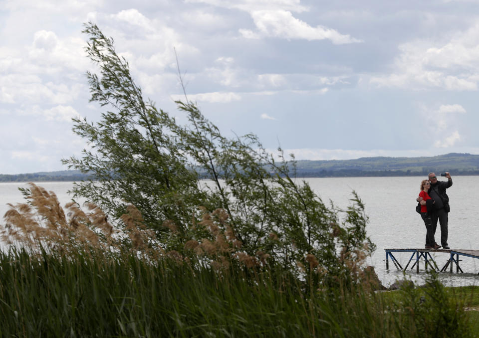 A couple stand on the pier over Lake Balaton in Szigliget, Hungary on May 18, 2021. Lake Balaton is the largest lake in Central Europe and one of Hungary's most cherished natural treasures. But some worry that the lake's fragile ecosystem and the idyllic atmosphere of the quaint villages dotted along its banks are in danger because of speculative developments. (AP Photo/Laszlo Balogh)