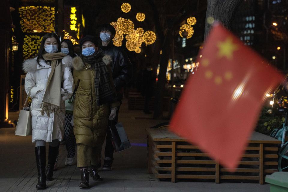 Patrons wearing masks to protect from the coronavirus past by a Chinese national flag as they visit a bar street on New Year Eve in Beijing on Thursday, Dec. 31, 2020. This New Year's Eve is being celebrated like no other, with pandemic restrictions limiting crowds and many people bidding farewell to a year they'd prefer to forget. (AP Photo/Ng Han Guan)