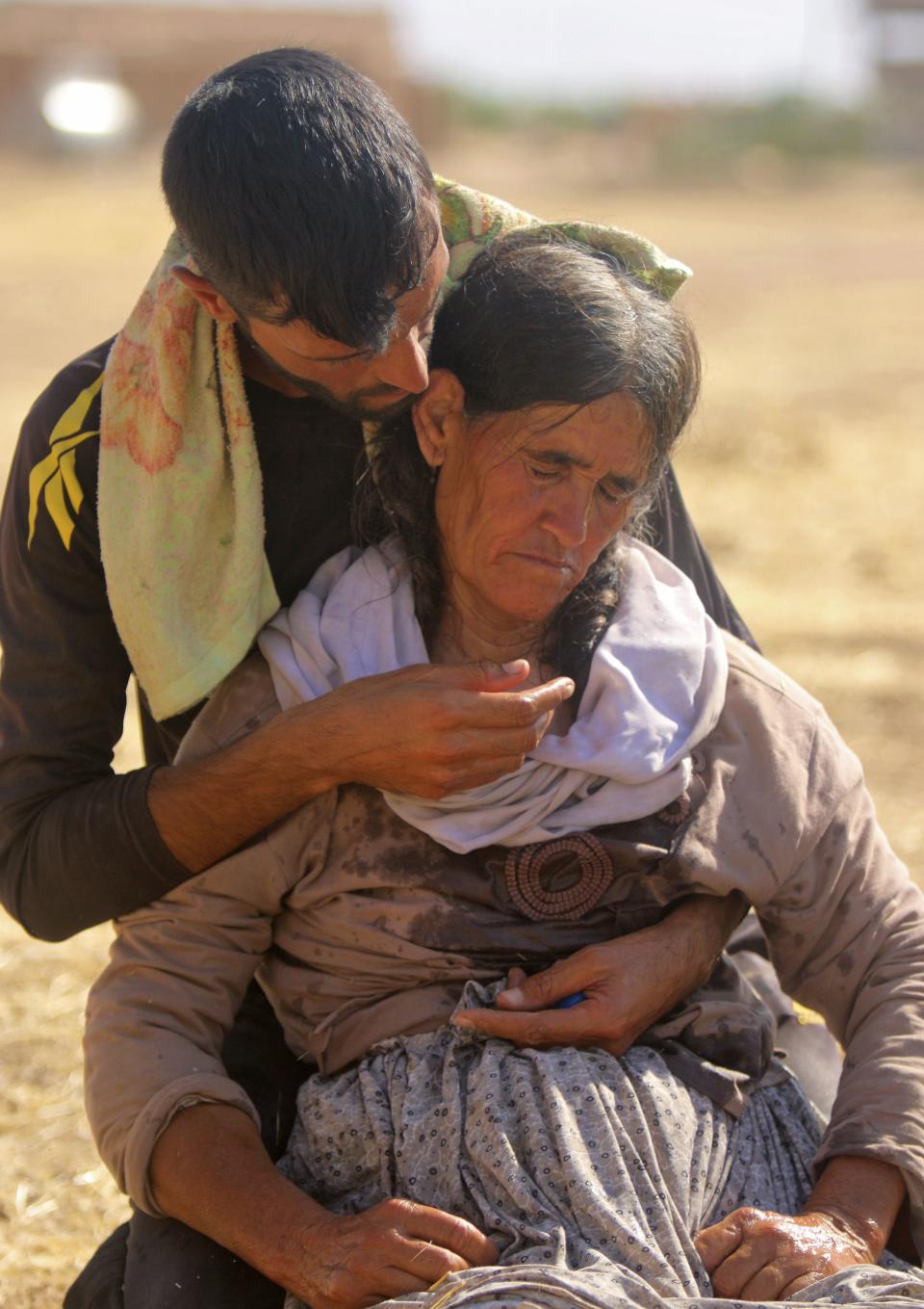 A displaced man helps a woman, both from the minority Yazidi sect fleeing violence from forces loyal to the Islamic State in Sinjar town, as they make their way towards the Syrian border, on the outskirts of Sinjar mountain, near the Syrian border