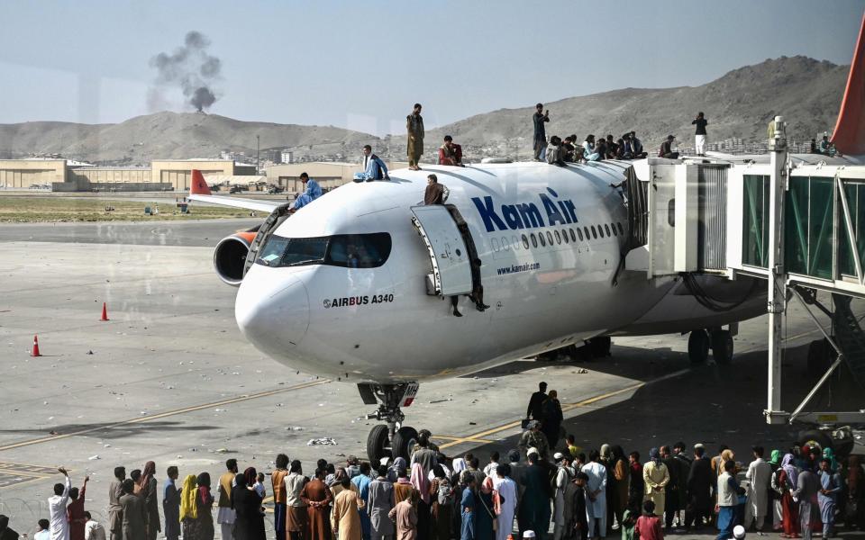 Afghan people climb atop a plane as they wait at the Kabul airport on Monday - Wakil Kohsar