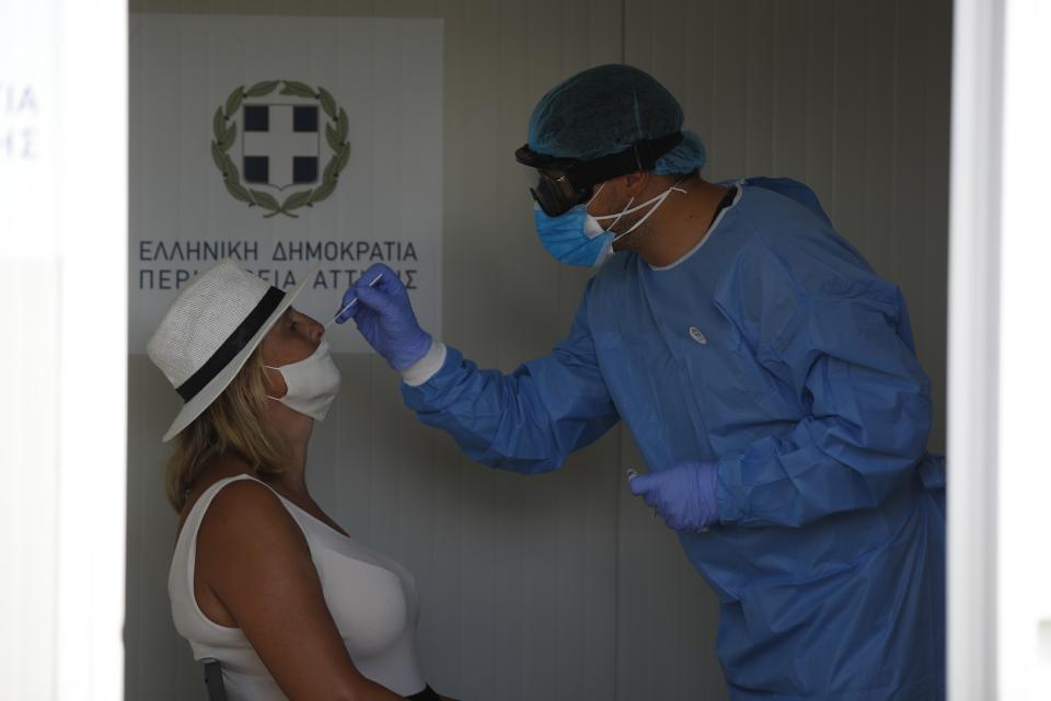 A medical worker wearing protective gear collects a swab from a traveller during a COVID-19 test after their arrival from a Greek island to the port of Piraeus, near Athens, Thursday, Aug. 20, 2020. Authorities in Greece are using free on-the-spot tests for ferry passengers and nightlife curfews on popular islands to stem a resurgence of the coronavirus after the country managed to dodge the worst of the pandemic. The number of confirmed virus cases and deaths in Greece remains lower than in many other European countries. (AP Photo/Thanassis Stavrakis)