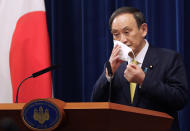 FILE - In this Dec. 4, 2020, file photo, Japanese Prime Minister Yoshihide Suga removes his face mask during a news conference in Tokyo. Opposition to the Tokyo Olympics is growing with calls for a cancellation as virus cases rise in Japan. The International Olympic Committee and local organizers have already said another postponement is impossible, leaving cancellation, or going ahead, as the only options. (AP Photo/Hiro Komae, Pool, File)