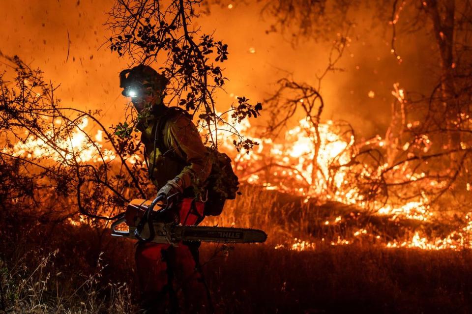 Ophir Hill volunteer firefighter Brian Harms works with a chainsaw to clear fuel from alongside Highway 174 while fighting the River Fire on Wednesday, Aug. 4, 2021, in Nevada County.