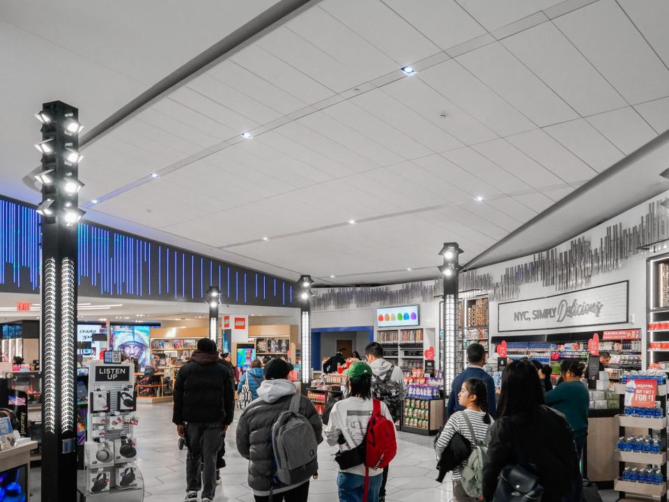 Inside an airport terminal with people walking toward a series of shops