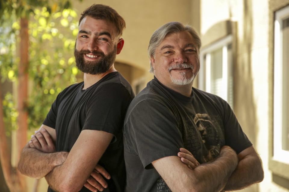 A younger and an older man, both smiling, stand back to back