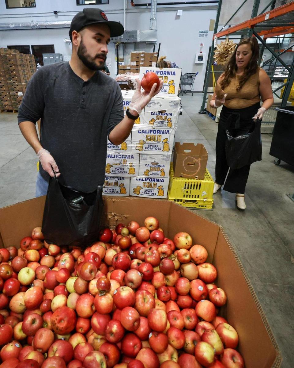 Cliff Mendez inspects apples while Kelly Boicourt checks sweet potatoes as SLO Food Bank volunteers and staff put together bags of produce on Dec. 5, 2023.