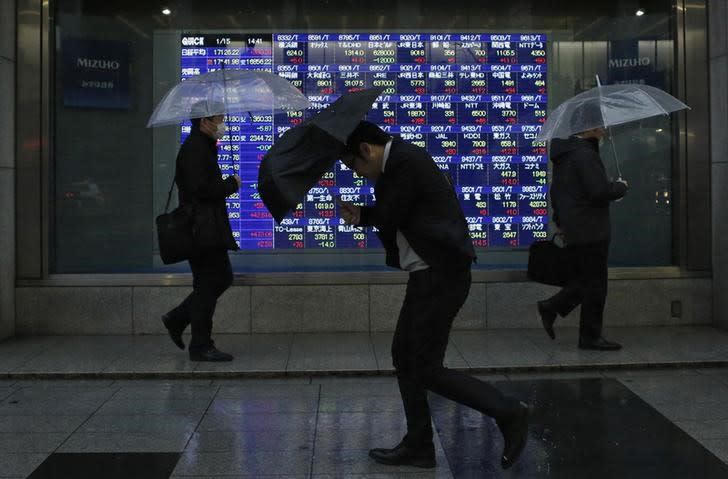 Pedestrians, holding umbrellas, walk past an electronic board showing stock prices outside a brokerage in Tokyo January 15, 2015. REUTERS/Yuya Shino