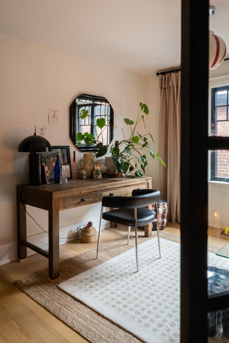 Wooden desk with black leather chair with large plant atop.