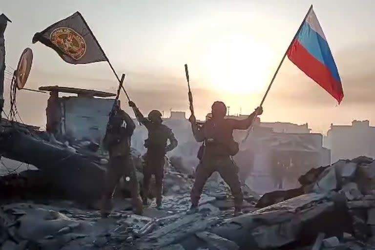 En esta imagen tomada de un video difundido por el Servicio de Prensa Prigozhin el sábado 20 de mayo de 2023, integrantes de la compañía militar Grupo Wagner de Yevgeny Prigozhin ondean una bandera rusa y otra del Grupo Wagner en una estructura dañada en Bájmut, Ucrania. (Servicio de Prensa Prigozhin vía AP)