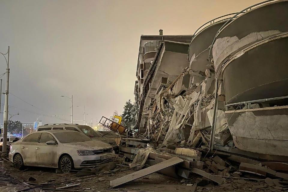 Damaged vehicles sit parked in front of a collapsed building following an earthquake in Diyarbakir, southeastern Turkey, early Monday, Feb. 6, 2023. A powerful quake has knocked down multiple buildings in southeast Turkey and Syria and many casualties are feared. (Depo Photos via AP)