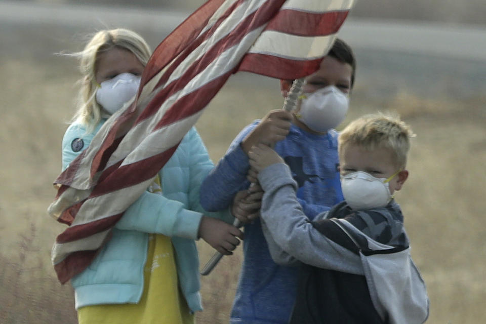 Niños sostienen una bandera de Estados Unidos a un lado de un camino al paso de la caravana del presidente Donald Trump por Chico, California, el sábado 17 de noviembre de 2018. El mandatario visito zonas afectadas por los incendios forestales en California. (AP Foto/Evan Vucci)