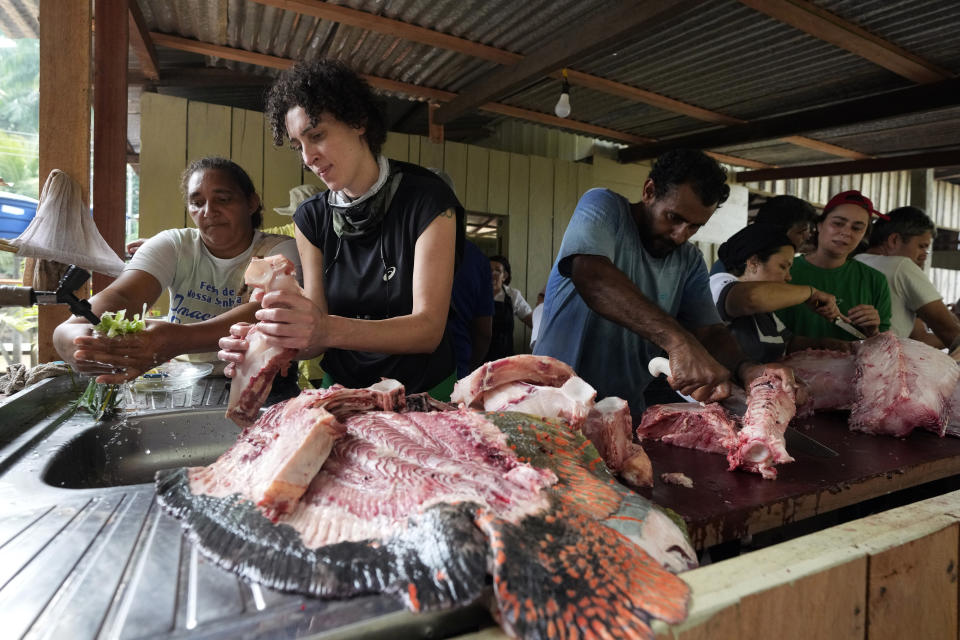 Priscila Deus De Olivera, second from left, prepares Pirarucu pieces to cook at San Raimundo settlement in Carauari, Brazil, Monday, Sept. 5, 2022. Indigenous communities working together with non-Indigenous riverine settlers manage the pirarucu in preserved areas of the Amazon. Most of it is exported, and the U.S. is the primary market. (AP Photo/Jorge Saenz)