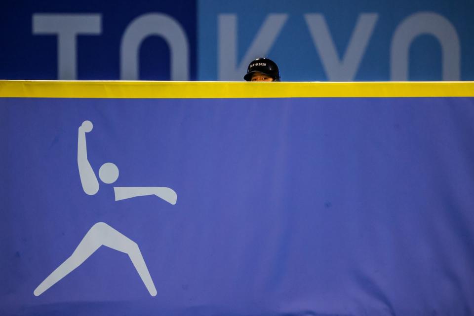 The hat and eyes of a person are visible over a barrier that has the logo of a softball pitcher.