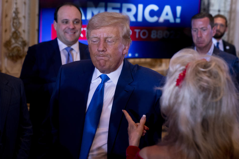 In a gilded state room, former President Donald Trump purses his lips in annoyance as a blonde guest, seen from behind, addresses him.