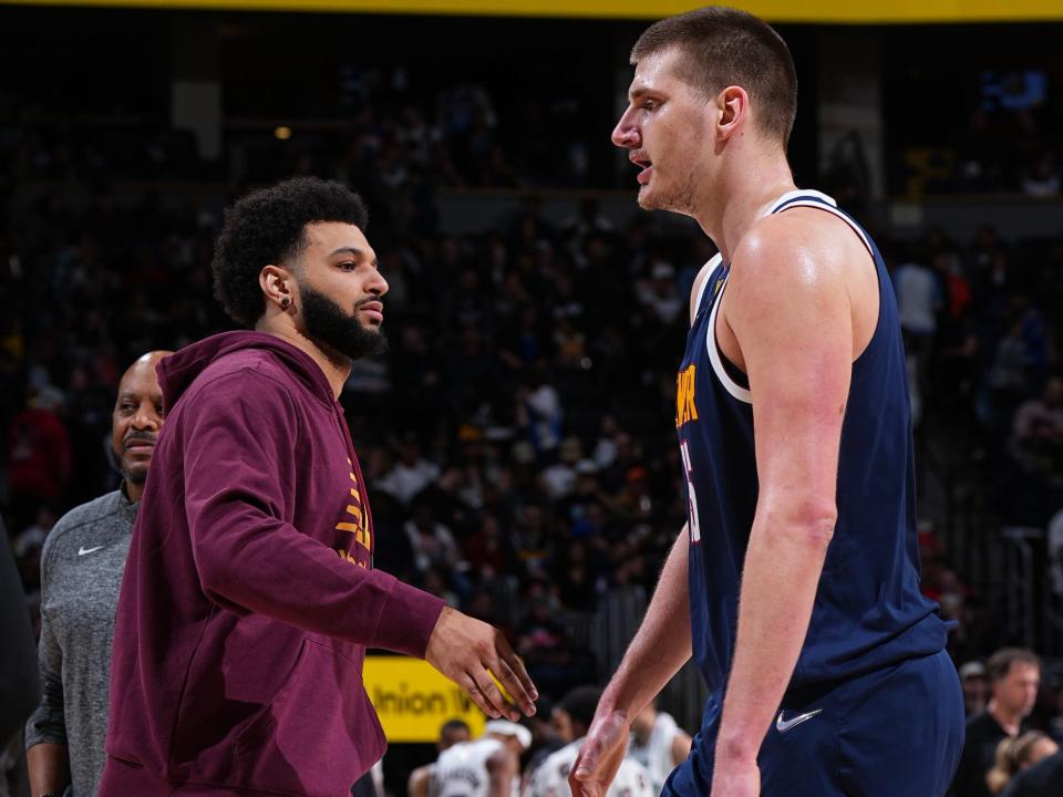 Jamal Murray, in street clothes, high-fives Nikola Jokic as he walks off the court during a game.