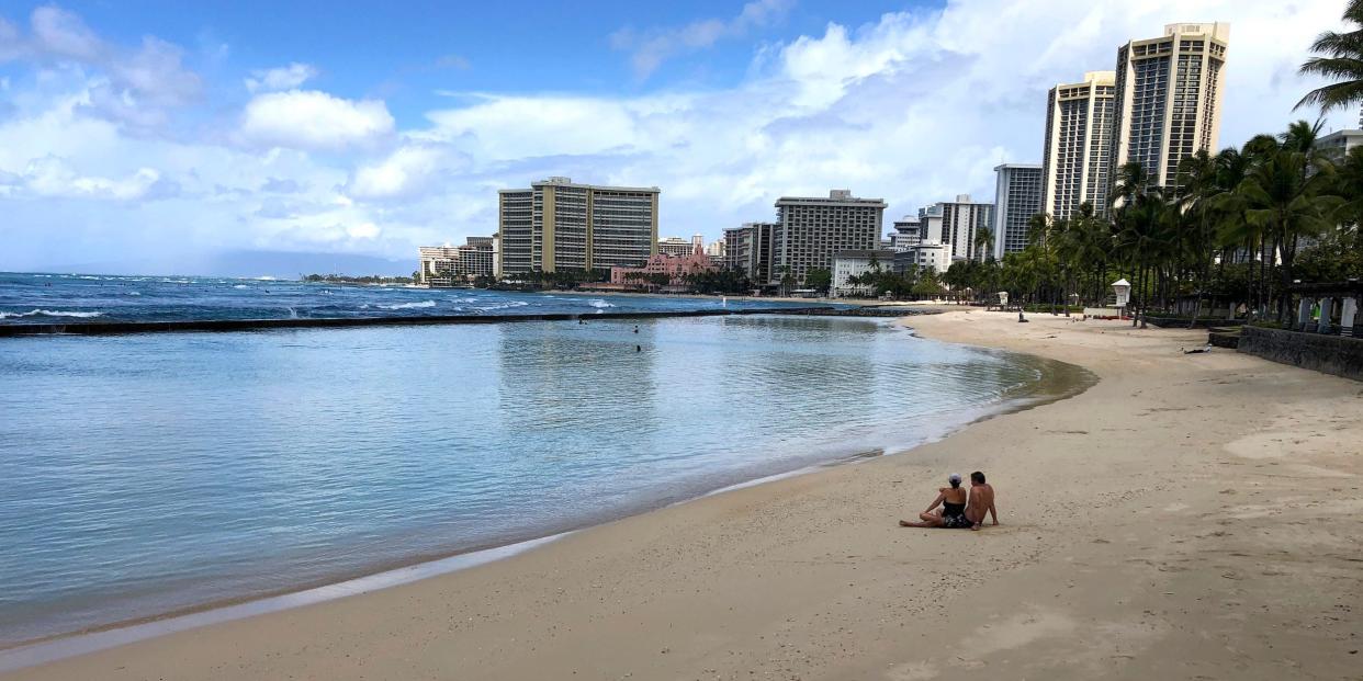 In this March 28, 2020, file photo, a couple sits on an empty section of Waikiki Beach in Honolulu. Hawaii law enforcement authorities are cracking down on rogue tourists who are visiting beaches, jetskiing, shopping and generally flouting strict requirements that they quarantine for 14 days after arriving.