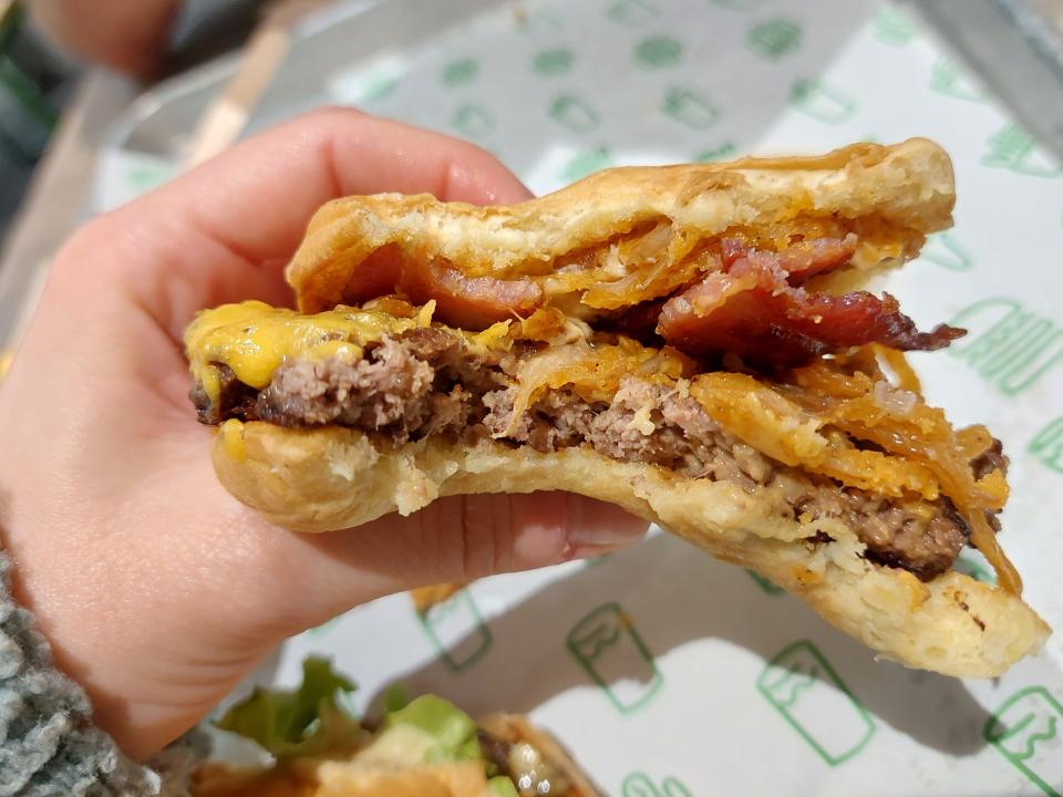 A ShackMeister burger from Shake Shack, being held in a hand and bitten into