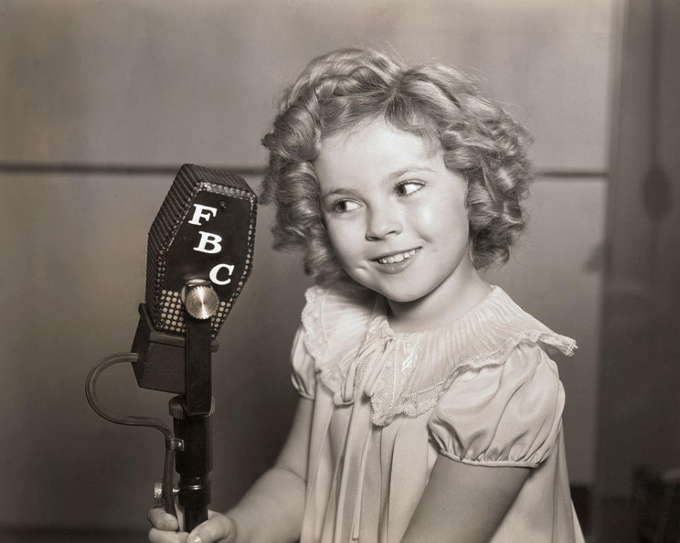 Shirley Temple as a child poses next to a microphone