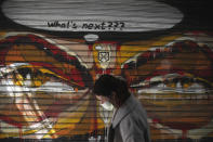 A woman wearing a face mask to protect against coronavirus, passes in front of graffiti painted on the shutter of a closed restaurant during a lockdown order by the Greek government to control the spread of the virus, in Athens, Monday, March 30, 2020. Greece's prime minister is calling on all his cabinet ministers and the lawmakers of his center-right New Democracy party to donate 50% of their salaries over the next two months to the fight against the spread of the new coronavirus. (AP Photo/Thanassis Stavrakis)