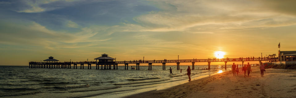 The pier at sunset looking calm and peaceful as people walk along the beach