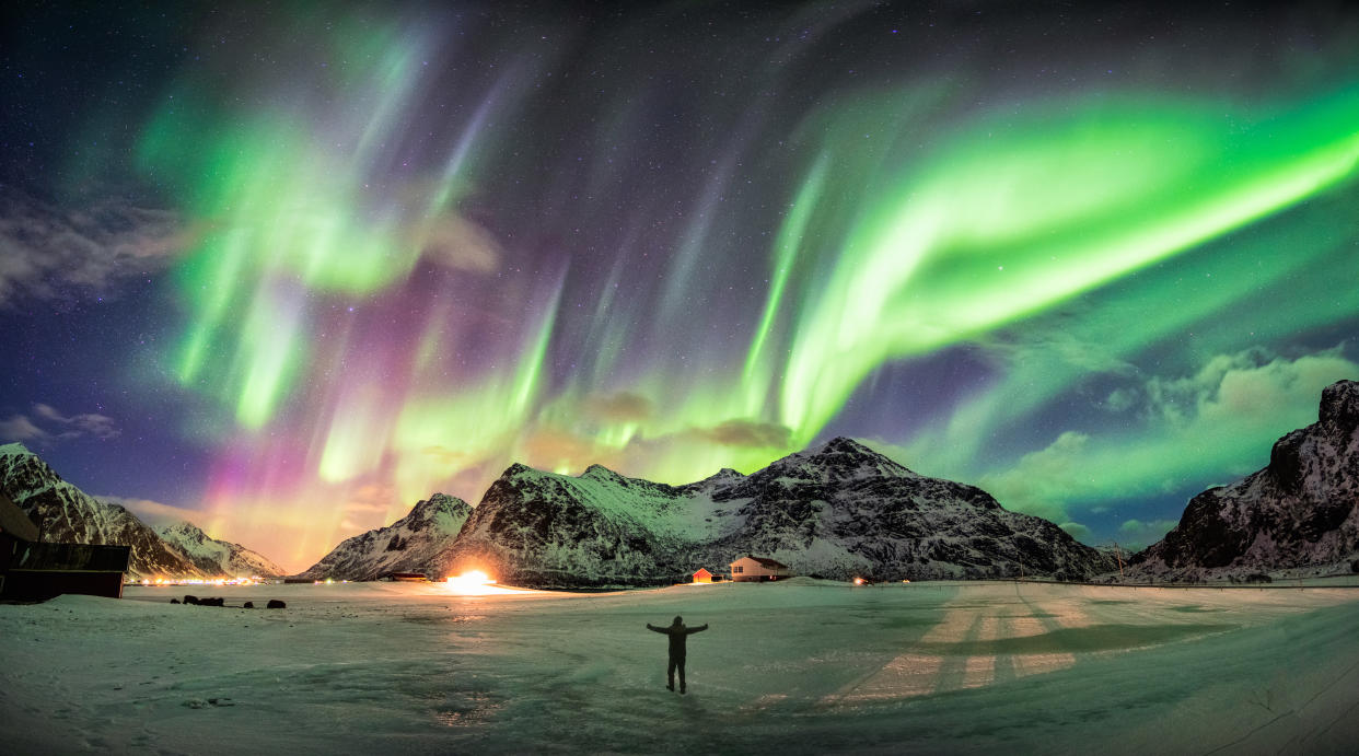 Aurora borealis (Northern lights) over mountain with one person at Skagsanden beach, Lofoten islands, Norway