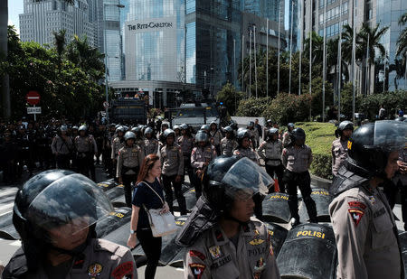 A woman walks near Indonesia policemen standing guard at Sudirman Business District area as members of the hardline group Islamic Defenders Front (FPI) march to the Indonesia police headquarters in Jakarta, Indonesia, January 23, 2017. REUTERS/Beawiharta