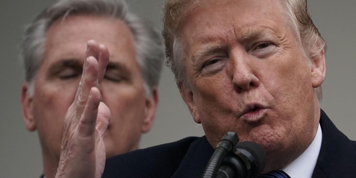 Then-US President Donald Trump, his lips pursed like he's blowing a kiss and his right hand raised as if in mid-karate chop, addresses reporters at the White House with House Minority Leader Kevin McCarthy, whose eyes are closed, standing in the background.