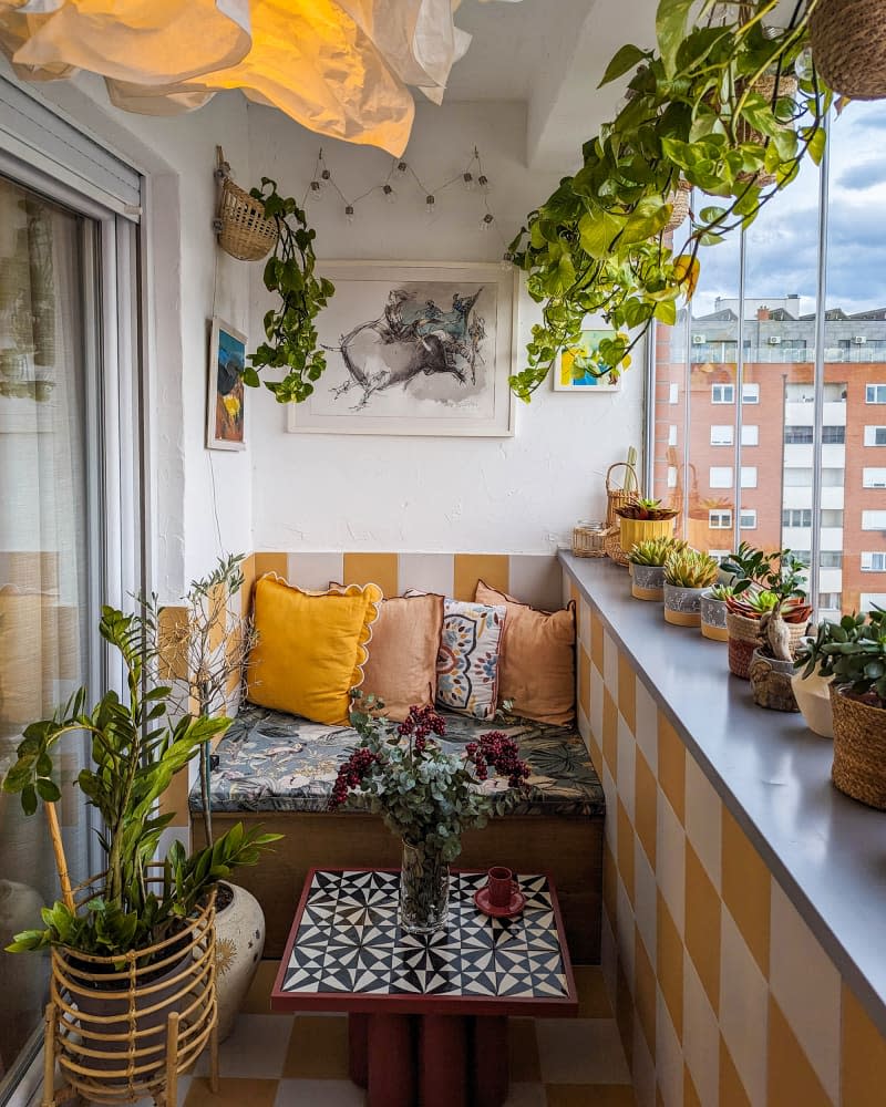 white sunroom with yellow and white checkered wall detail, fabric nestled bench, hanging and potted plants