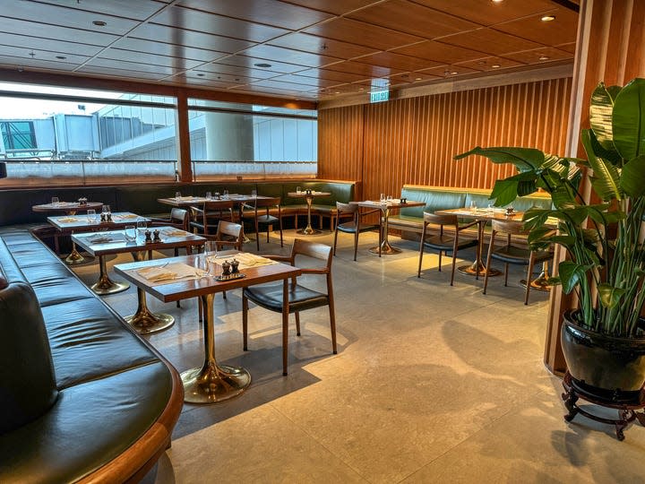 An interior shot shows the restaurant at Cathay Pacific's The Pier, a first- class lounge at Hong Kong International Airport. Wood panels, green accents and mid-century inspired designs fill the space.