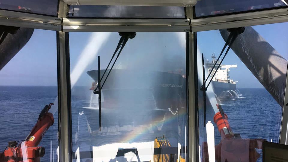 In this photo dated Thursday June 13, 2019, made available by the Norwegian shipowner Frontline, showing the crude oil tanker Front Altair seen through glass observation window as water cannon operate during the firefighting of the fire onboard the Norwegian ship in the Gulf of Oman. The U.S. Navy rushed to assist the stricken vessels in the Gulf of Oman, off the coast of Iran, as two oil tankers came under suspected attack amid heightened tension between Iran and the U.S. (Frontline via AP)