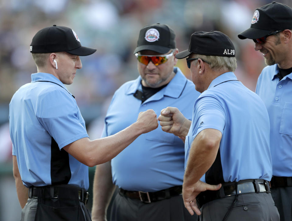 Home plate umpire Brian deBrauwere, left, huddles with officials while wearing an earpiece connected to a ball and strikes calling system prior to the start of the Atlantic League All-Star minor league baseball game, Wednesday, July 10, 2019, in York, Pa. deBrauwere wore the earpiece connected to an iPhone in his ball bag which relayed ball and strike calls upon receiving it from a TrackMan computer system that uses Doppler radar. The independent Atlantic League became the first American professional baseball league to let the computer call balls and strikes during the all star game. (AP Photo/Julio Cortez)