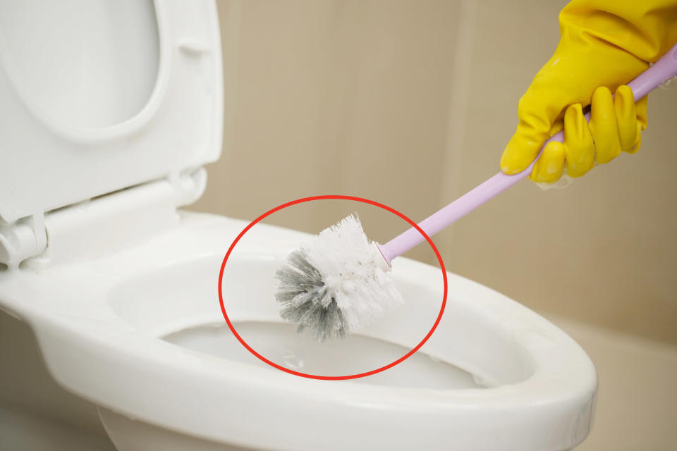 A rubber-gloved hand holding a toilet brush positioned above a toilet as if about to clean it