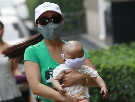 A woman carrying a baby, both wearing masks, make their way down a street in Binhai new district, more than five kilometers (3 miles) away from the site of last week's explosions, in Tianjin, China, August 17, 2015. REUTERS/Kim Kyung-Hoon